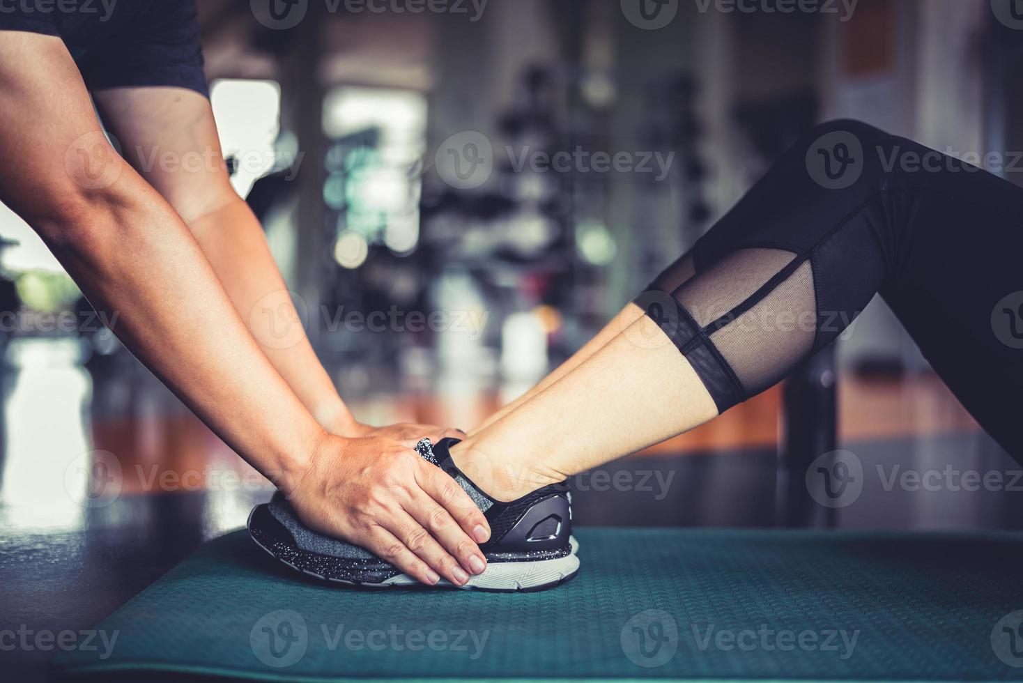 le mani dell'istruttore di fitness aiutano la donna in forma ad allenare il crunch twist foto
