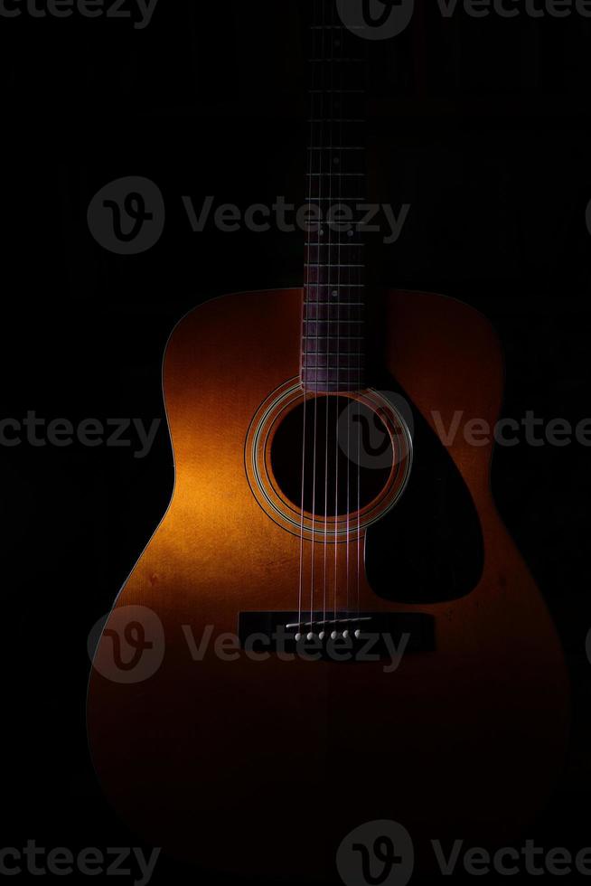 dettaglio di chitarra acustica su sfondo nero tra luci o ombre foto