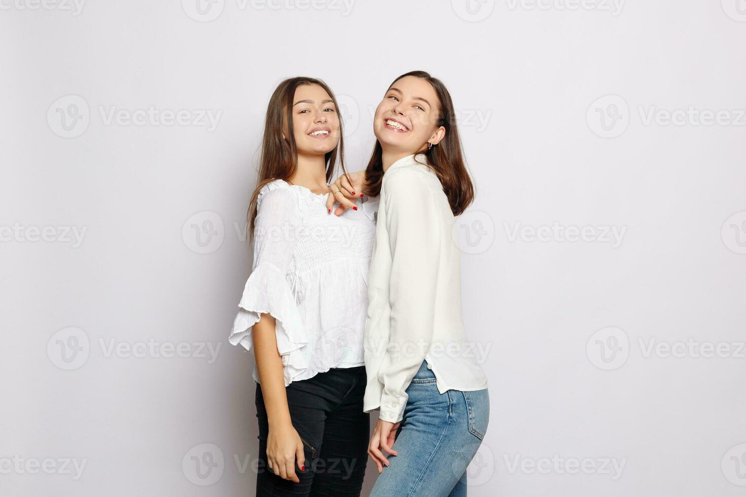 Due ridendo ragazze nel bianca vuoto magliette guardare in il telecamera foto