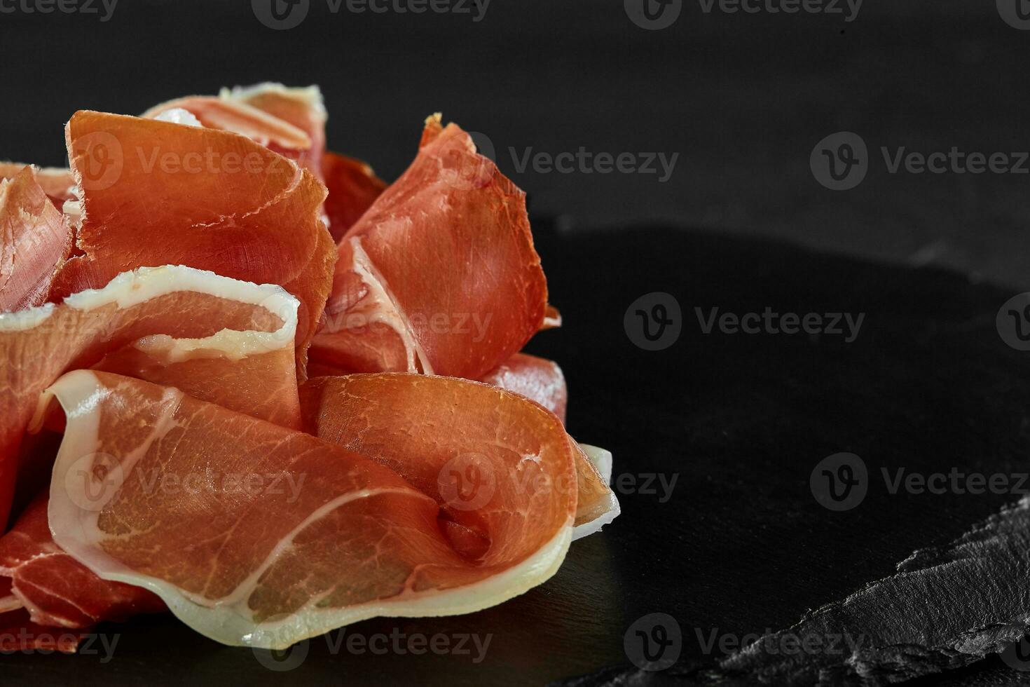 buongustaio, manualmente affettato jamon su nero pietra ardesia tavola contro un' buio grigio sfondo. avvicinamento sparo. lato Visualizza. copia spazio. foto