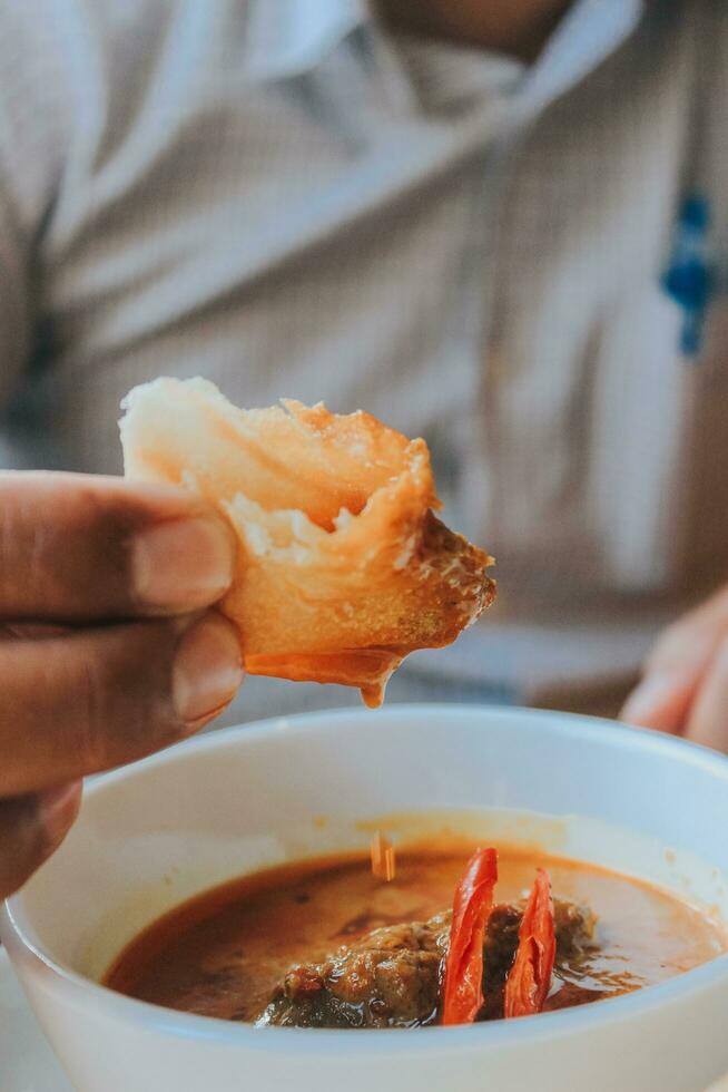 persone mangiare pollo curry, kerala stile pollo curry utilizzando fritte Noce di cocco nel tradizionale modo e disposte nel un' nero ceramica nave quale è posto su un' grafite foglio foto