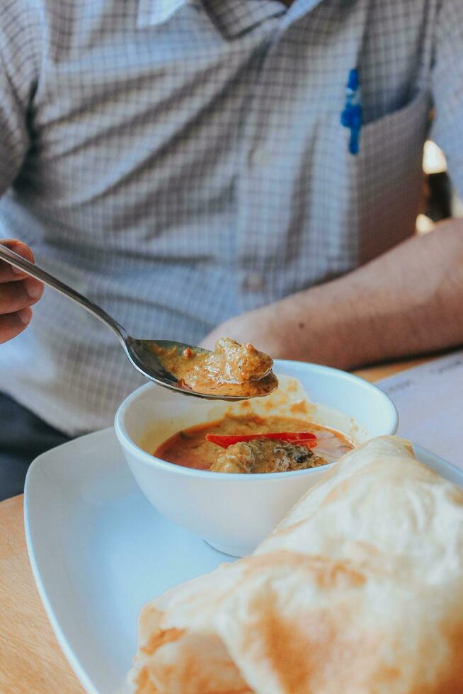 persone mangiare pollo curry, kerala stile pollo curry utilizzando fritte Noce di cocco nel tradizionale modo e disposte nel un' nero ceramica nave quale è posto su un' grafite foglio foto