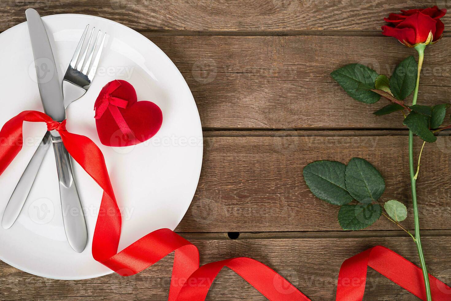 san valentino giorno tavolo ambientazione con piatto, forchetta, coltello, rosso cuore, nastro e rosa. sfondo foto