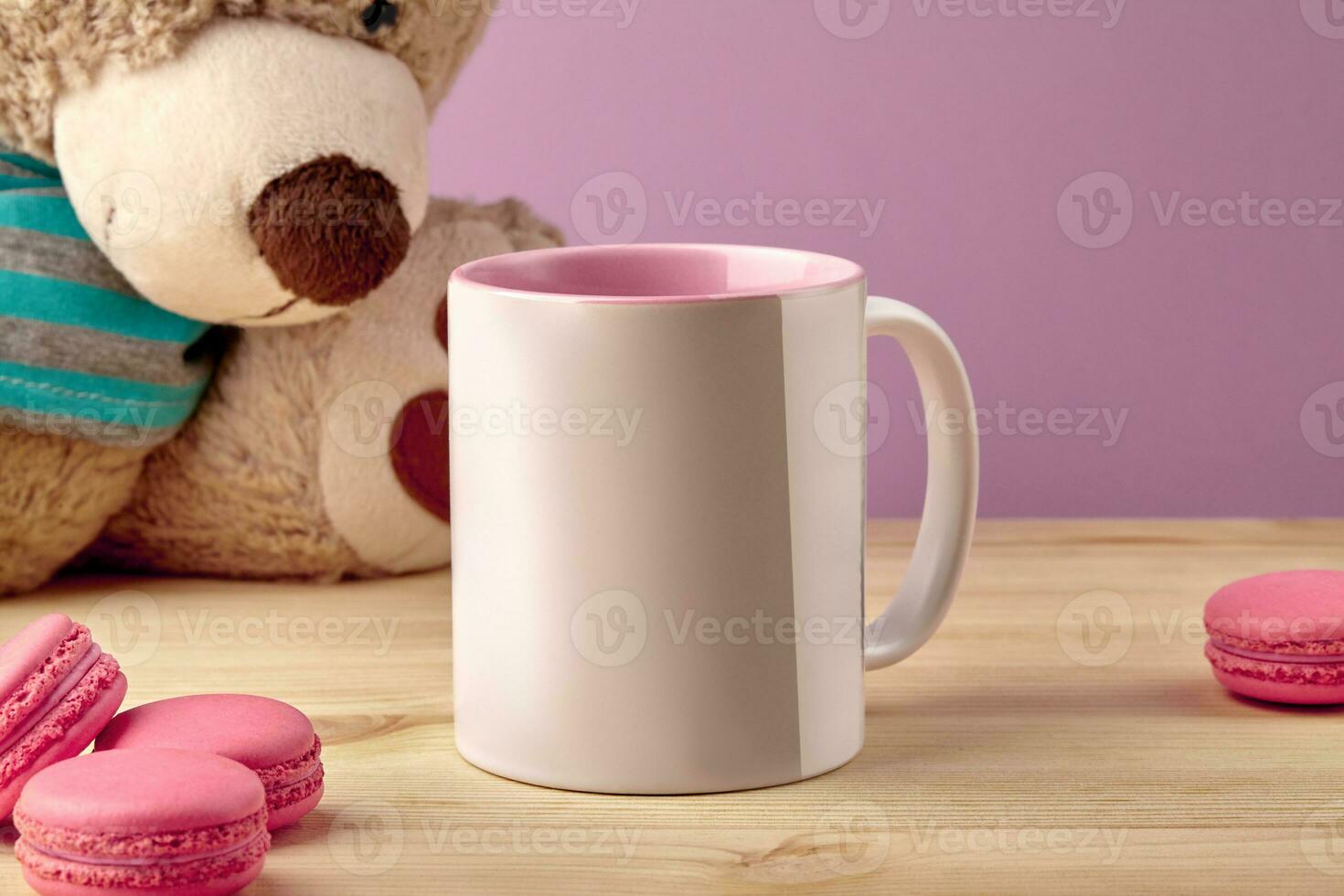 bianca porcellana boccale per caffè o tè su di legno del desktop Il prossimo per giocattolo orsacchiotto orso e macarons contro rosa studio sfondo. vicino su, copia spazio foto