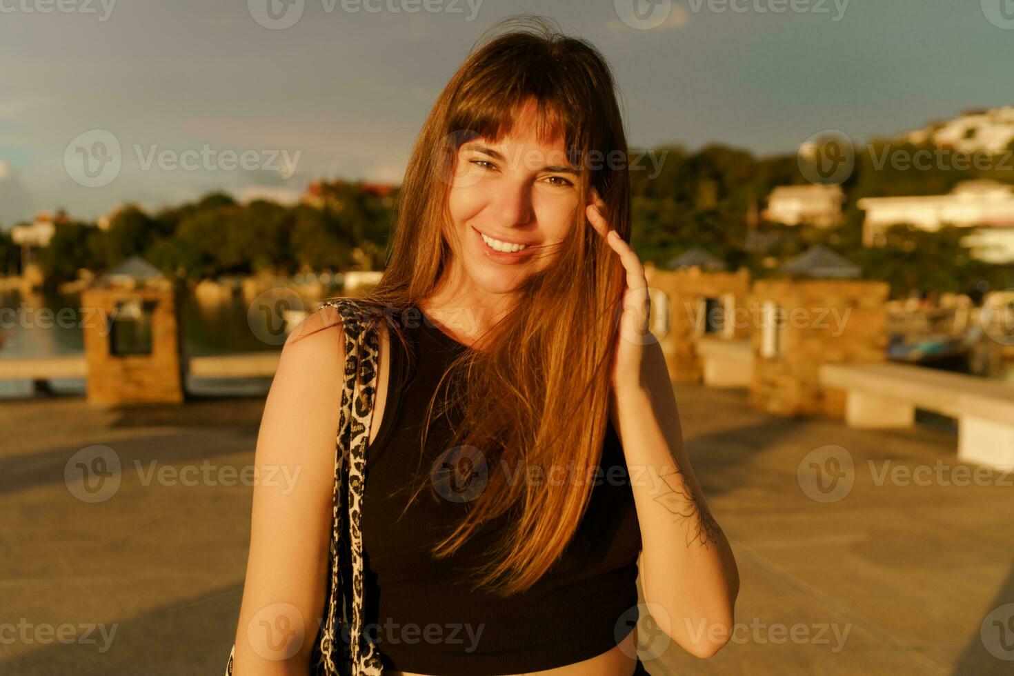 bellissimo brunetta donna con elegante acconciatura a piedi all'aperto su il molo. caldo sunser colori. viaggio e vacanza concetto. foto