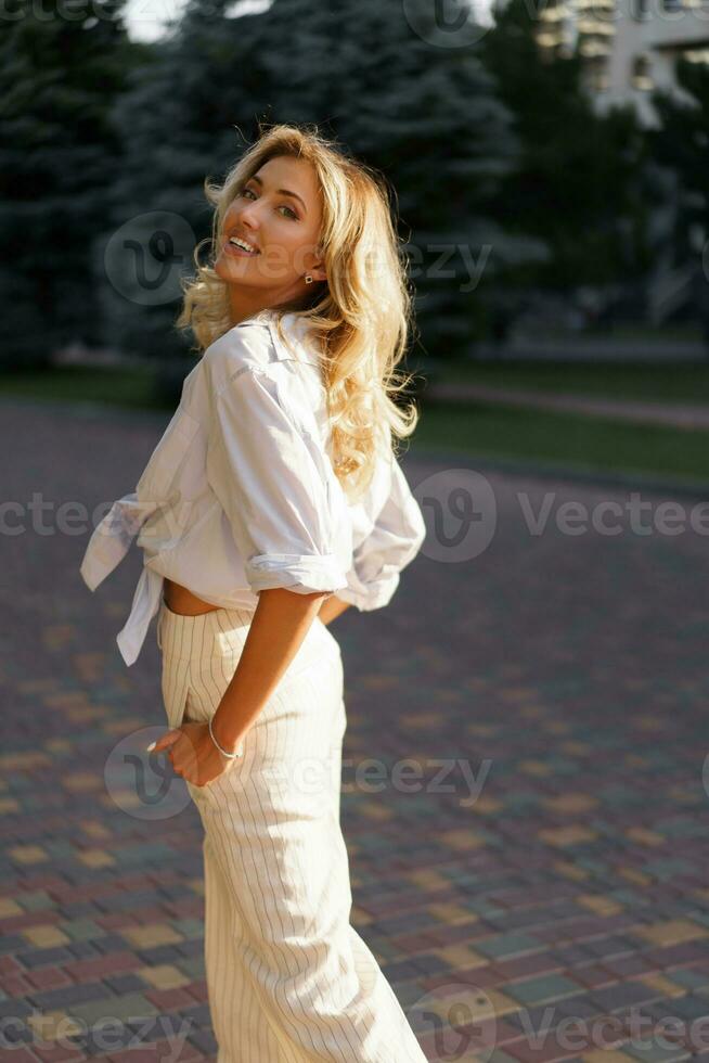 bellissimo biondo donna nel elegante moda casuale attrezzatura in posa su il strada. caldo tramonto colore. foto