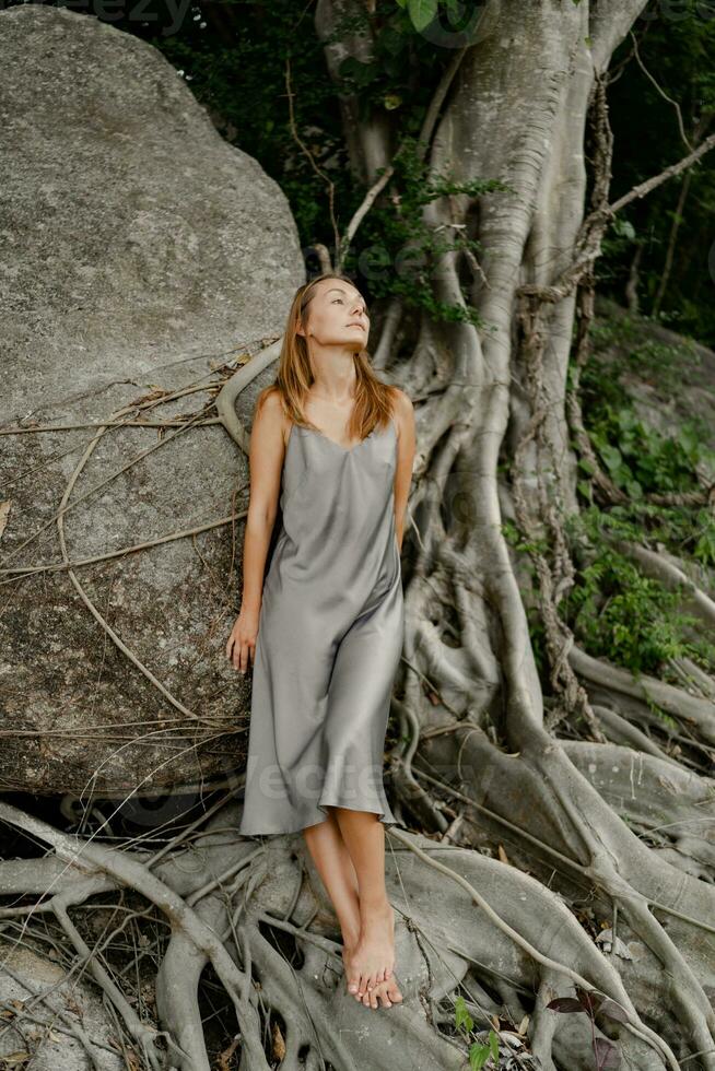 elegante brunetta donna nel seta grigio vestito in posa nel su il rocce. foto