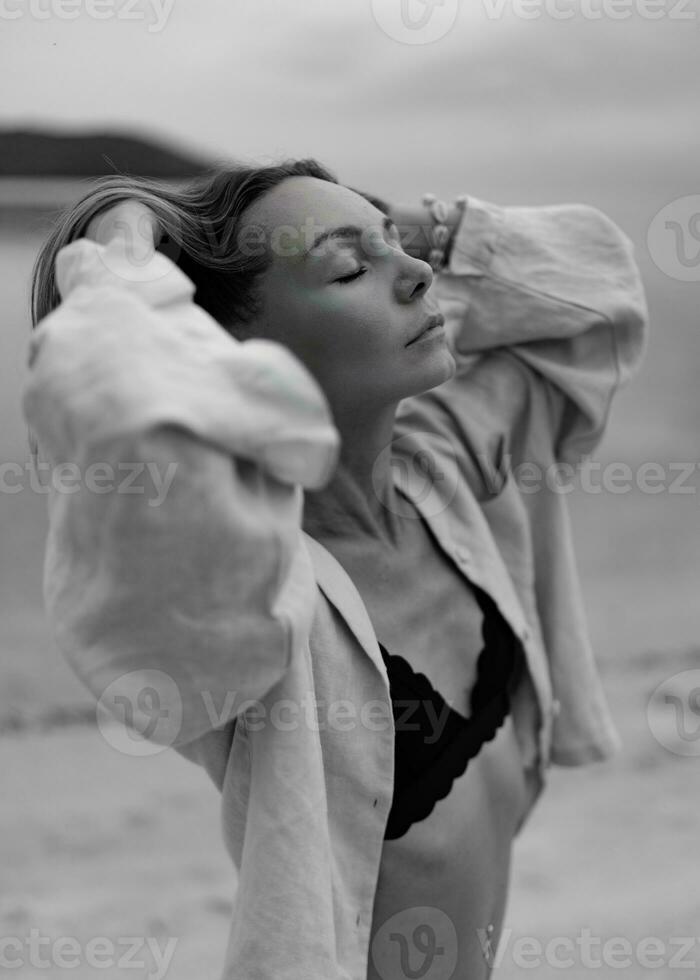 elegante donna nel casuale attrezzatura in posa su solitario spiaggia nel nuvoloso tempo atmosferico. nero e bianca. foto