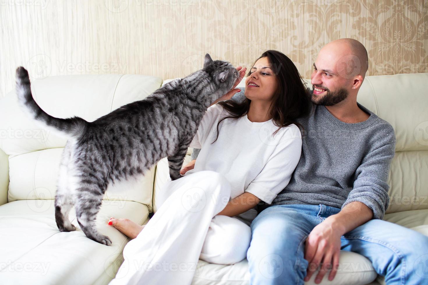 giovane uomo e donna con il loro gatto sul divano di casa foto