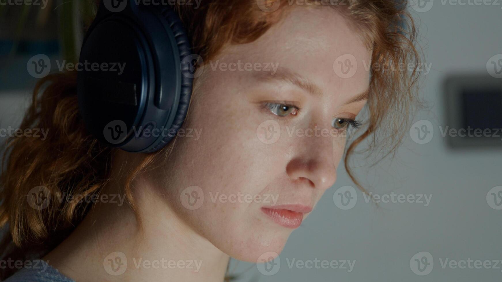 giovane donna bianca in cuffia, la luce dello schermo si riflette sugli occhi foto