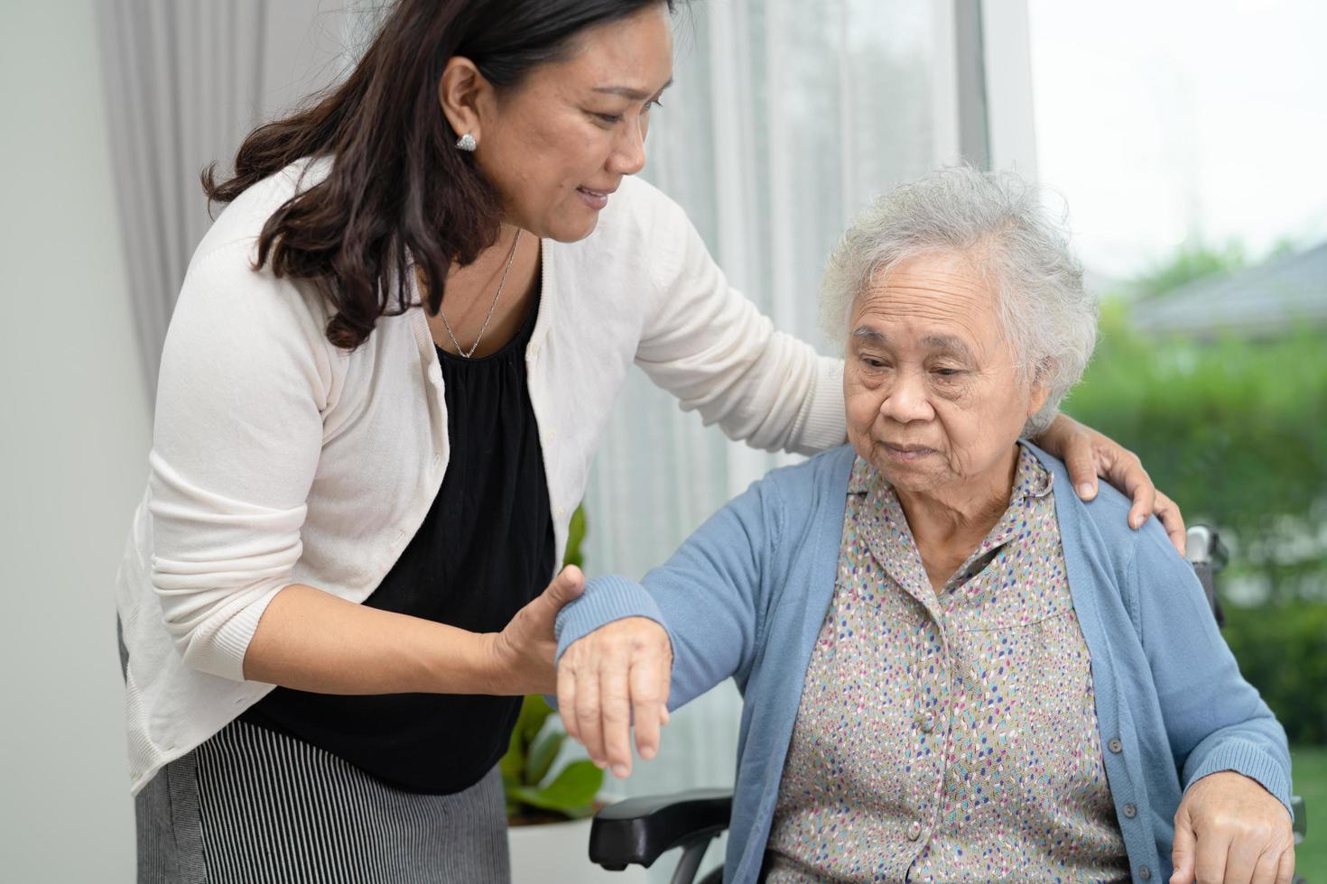 aiutare e prendersi cura di una donna anziana asiatica seduta su una sedia a rotelle foto