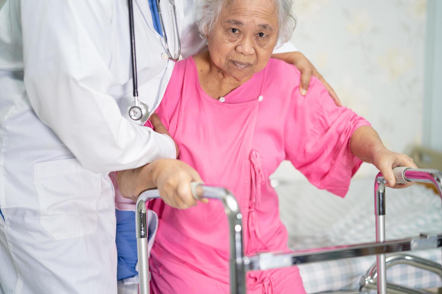 cura del medico asiatico, aiuto e supporto a piedi del paziente anziano con il deambulatore foto