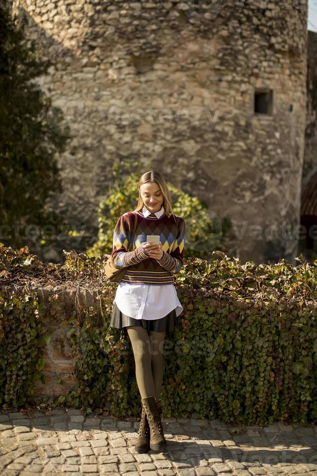 bella giovane donna in piedi con il telefono cellulare in strada al giorno d'autunno foto