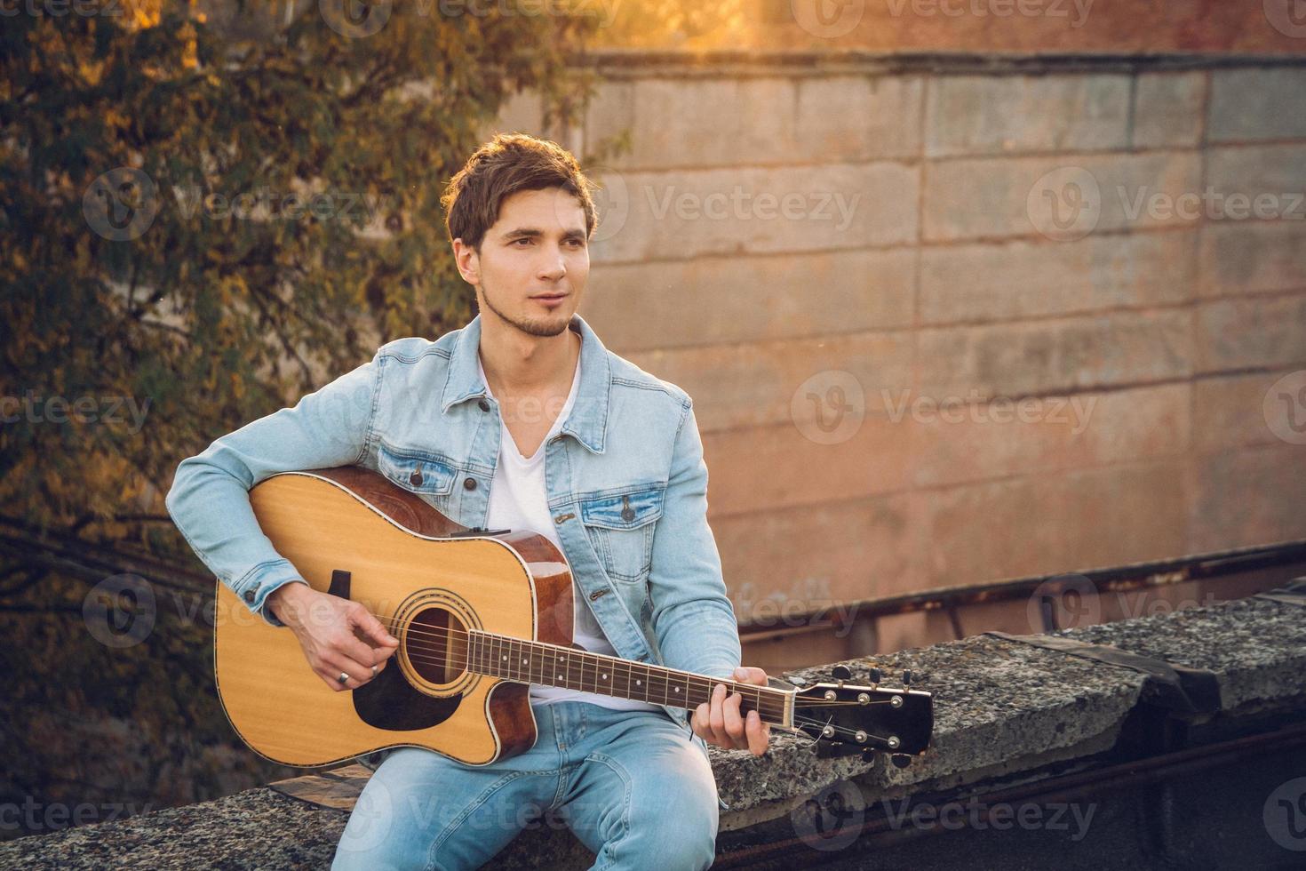 giovane che suona la chitarra in città sullo sfondo dei raggi del sole foto