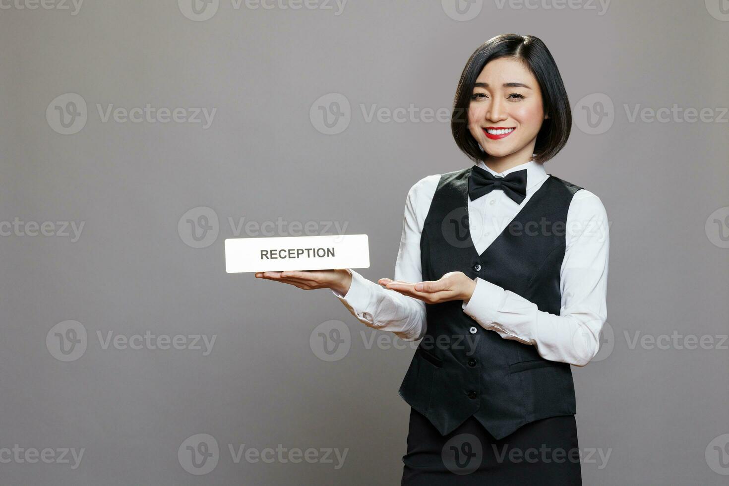 ristorante addetto alla reception in mostra ricezione acciaio piatto, sorridente e guardare a telecamera con contento espressione. Hotel asiatico donna lavoratore mostrando tavolo cartello studio ritratto foto