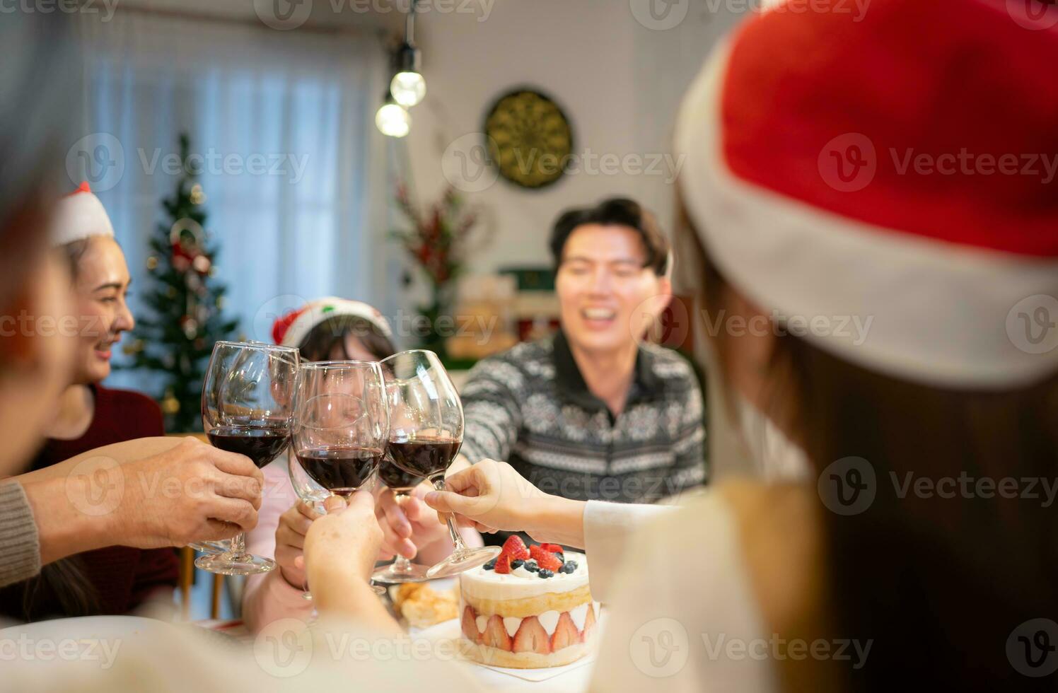 contento asiatico famiglia festeggiare Natale insieme a casa. allegro anziano genitori e bambini nel Santa cappello tintinnante bicchieri di rosso vino. foto