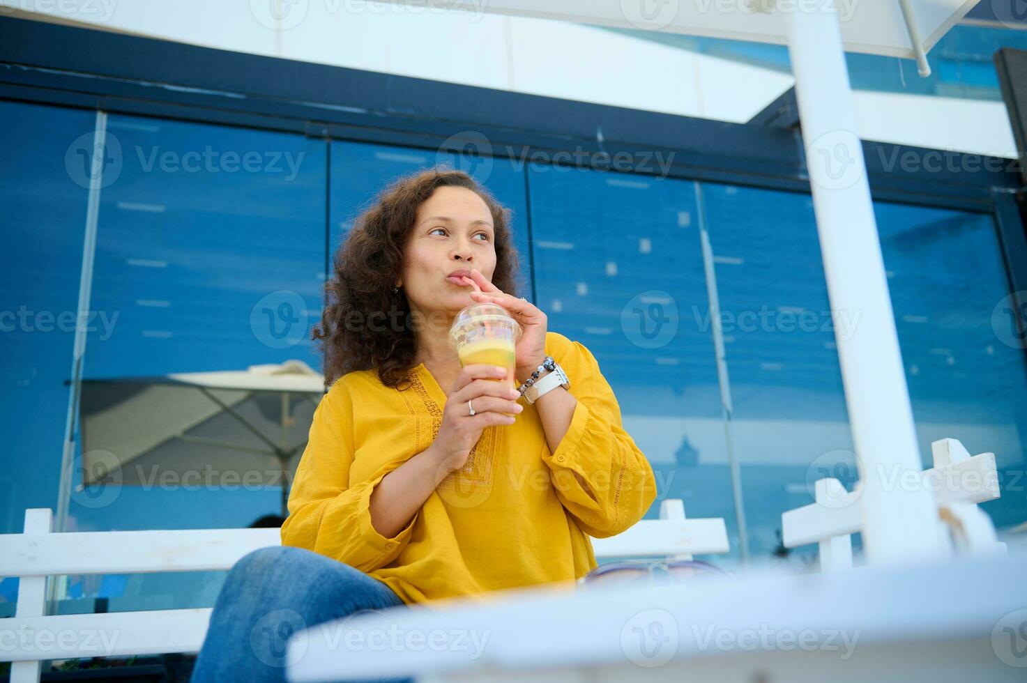 latino americano affascinante giovane adulto donna potabile fresco salutare succo, seduta su un' estate terrazza di un all'aperto bar. foto