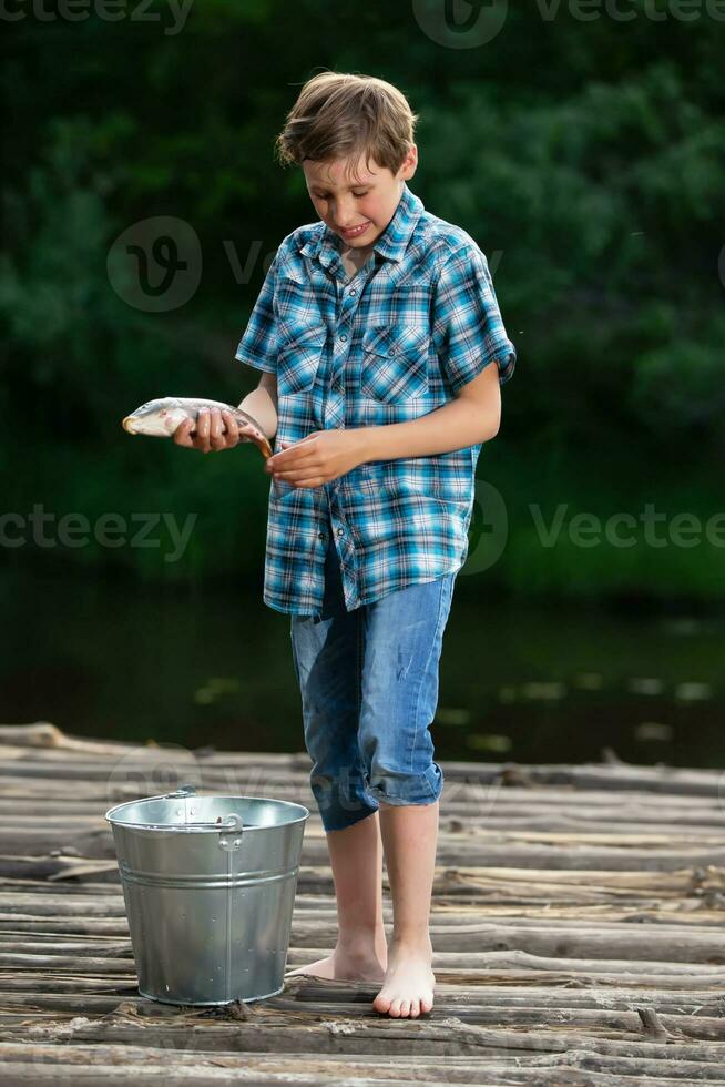 un' pescatore ragazzo ammira il suo presa. pesca bambino. foto