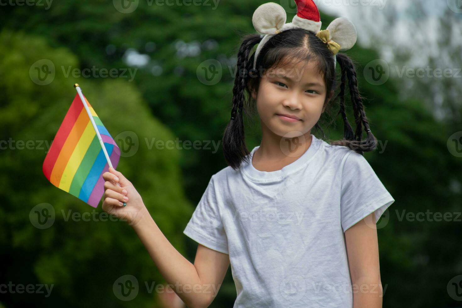 asiatico carino ragazza Tenere arcobaleno bandiera, lgbt simbolo, sfocato parco sfondo, concetto per lgbt persone celebrazione nel orgoglio mese in giro il mondo. foto