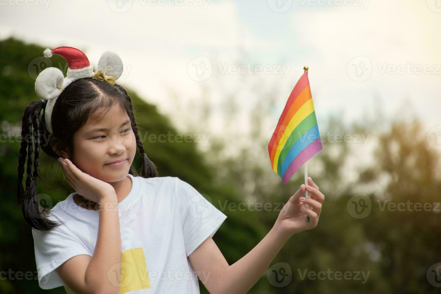 asiatico carino ragazza Tenere arcobaleno bandiera, lgbt simbolo, sfocato parco sfondo, concetto per lgbt persone celebrazione nel orgoglio mese in giro il mondo. foto