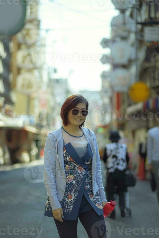 asiatico donna trentadue denti sorridente viso in piedi nel dotonbori strada uno di maggior parte popolare in viaggio destinazione nel osaka Giappone foto