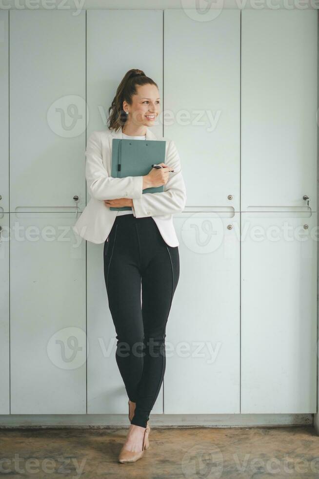 riuscito donna d'affari in piedi nel creativo ufficio e guardare al di fuori finestre. donna imprenditore nel un' coworking spazio sorridente. foto