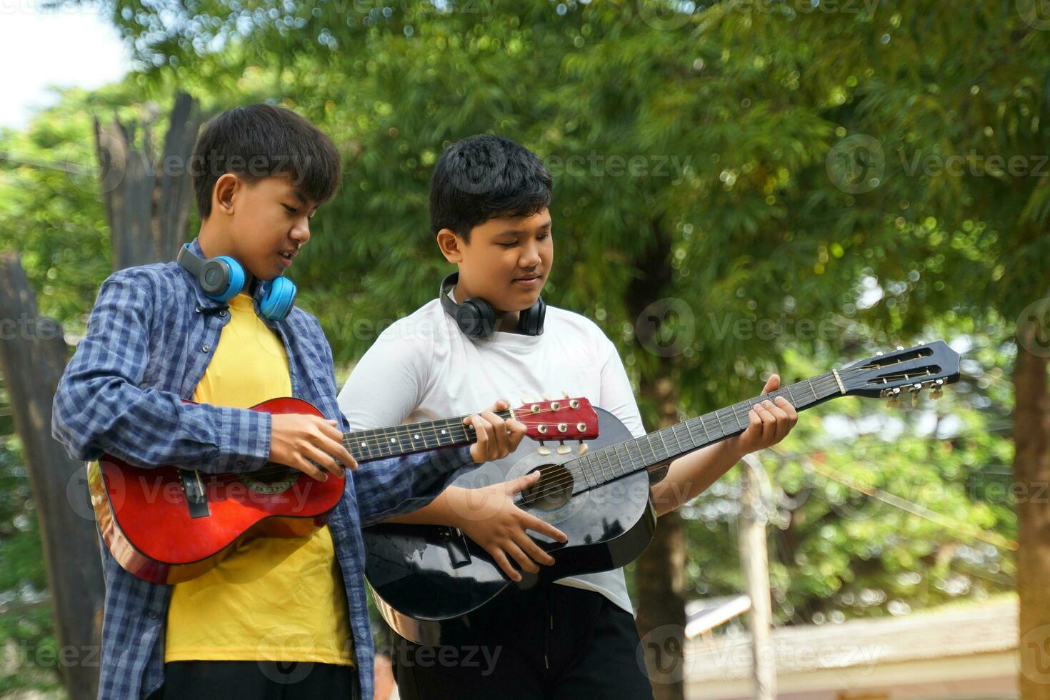 Due asiatico ragazzi erano avendo divertimento giocando classico chitarra insieme durante loro gratuito tempo a un' scuola estate campo a il parco. morbido e selettivo messa a fuoco. foto