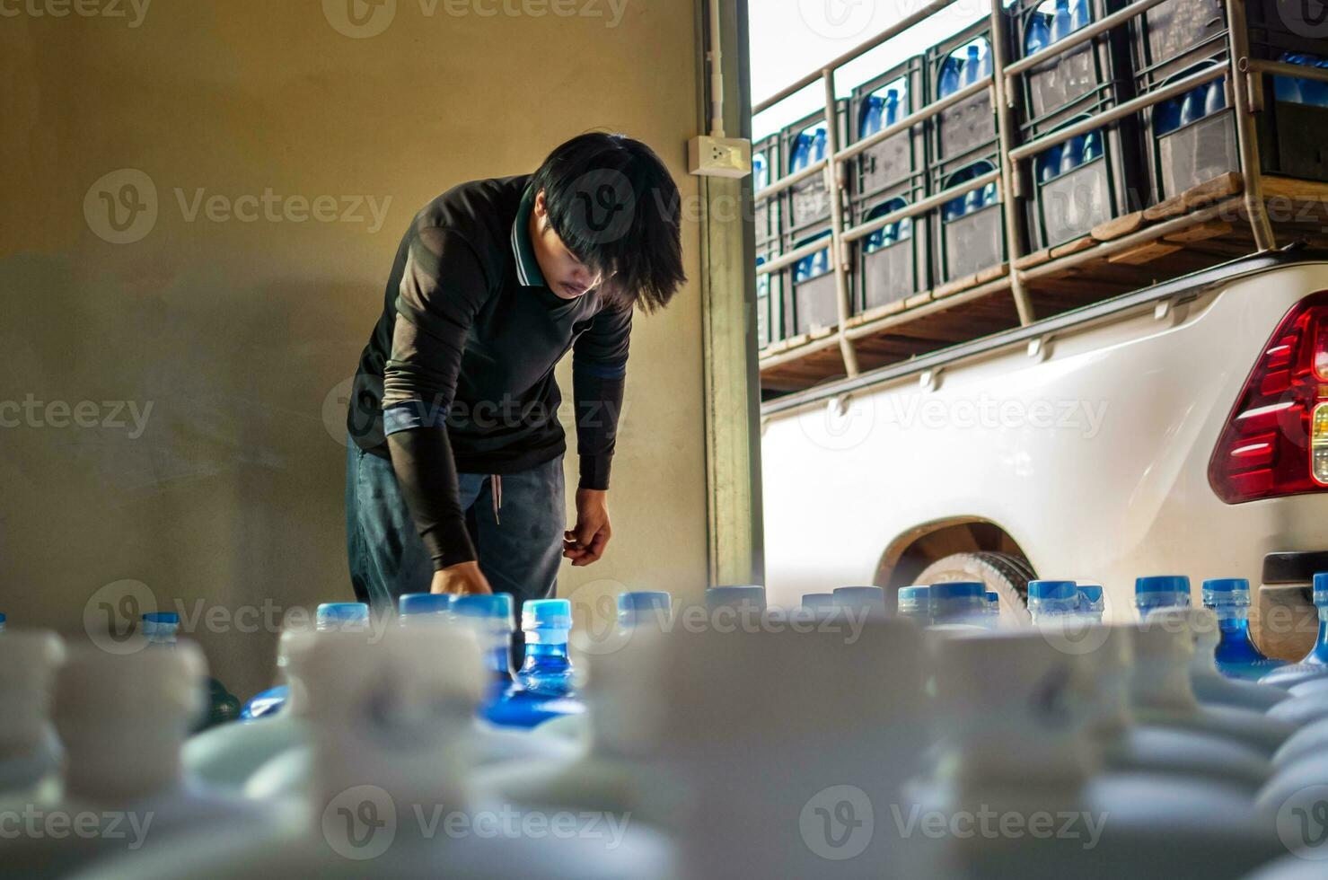 lavoratori sollevamento potabile acqua chiaro e pulito nel blu plastica gallone in il indietro di un' trasporto camion purificato potabile acqua dentro il produzione linea per preparare per vendita.piccolo attività commerciale foto