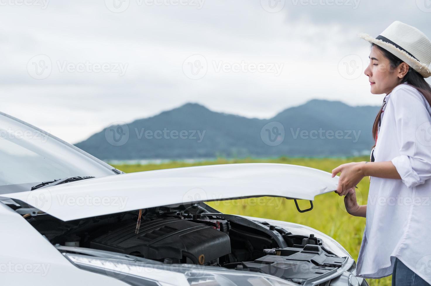 donna asiatica che apre il cofano dell'auto per riparare l'auto rotta in panne foto