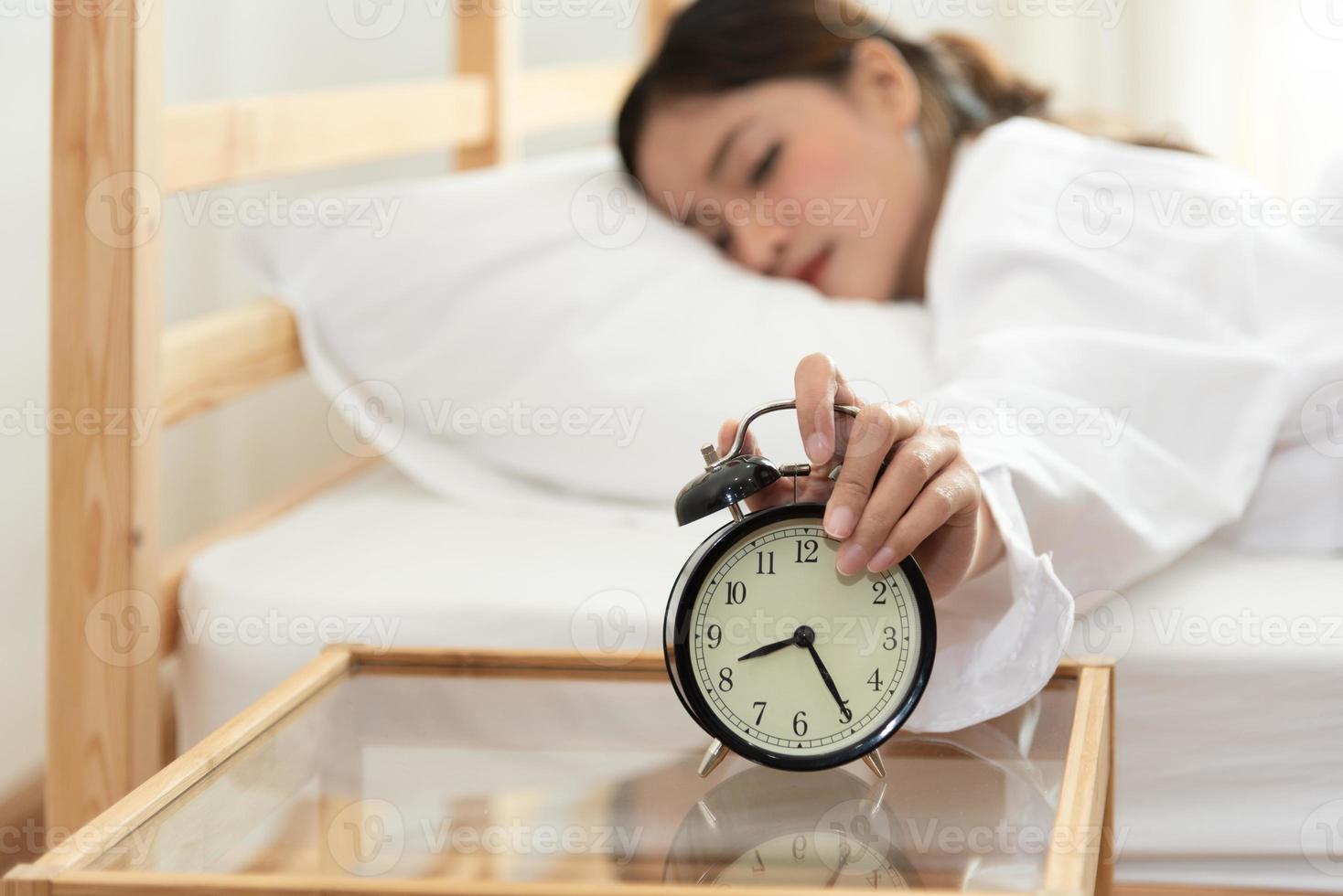 giovane donna asiatica di bellezza che spegne la sveglia in tarda mattinata foto