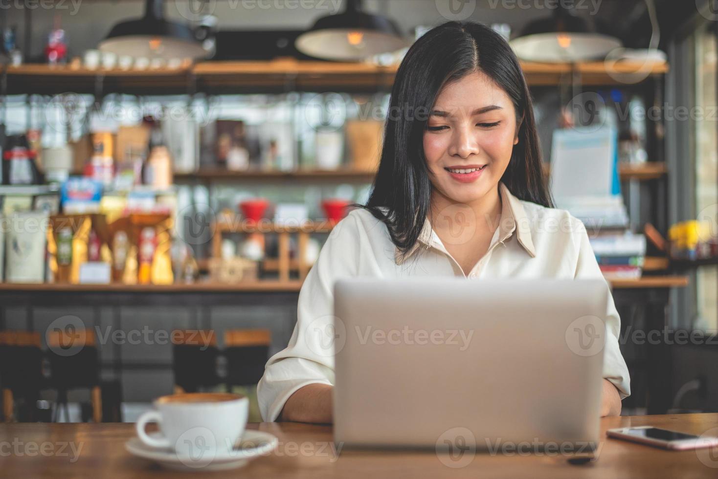 freelancer femminile asiatico che sorride quando si utilizza il computer portatile in cafe foto