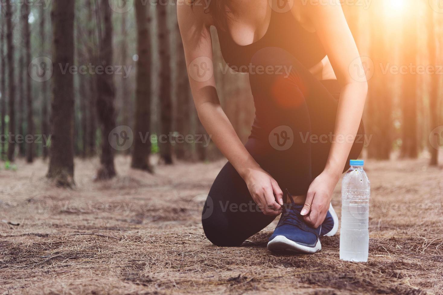 donna che allaccia i lacci delle scarpe quando fa jogging nella foresta indietro foto