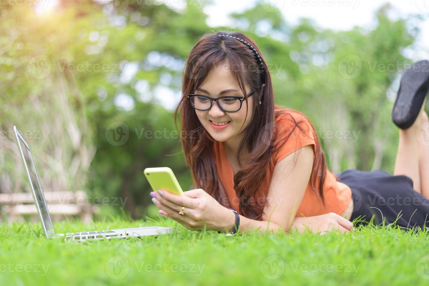 donna asiatica felice che utilizza smartphone quando si rilassa nel parco foto