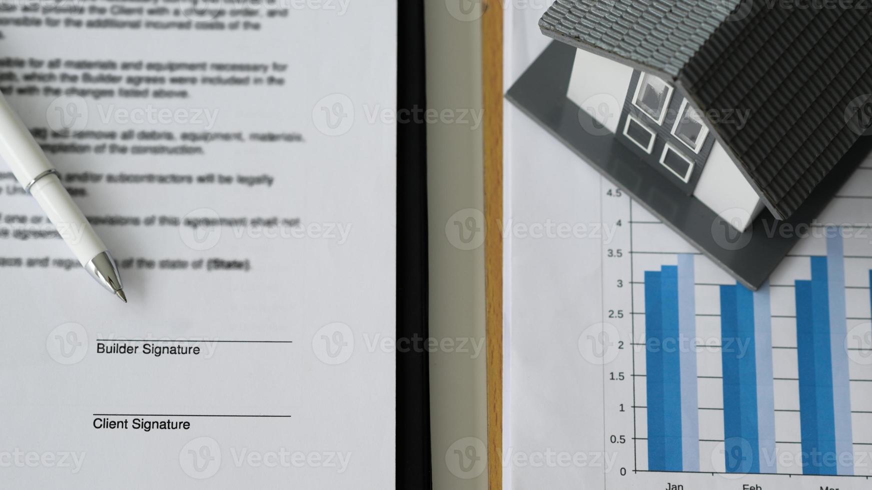 penna posta su documenti contrattuali e case modello su grafici di dati. foto