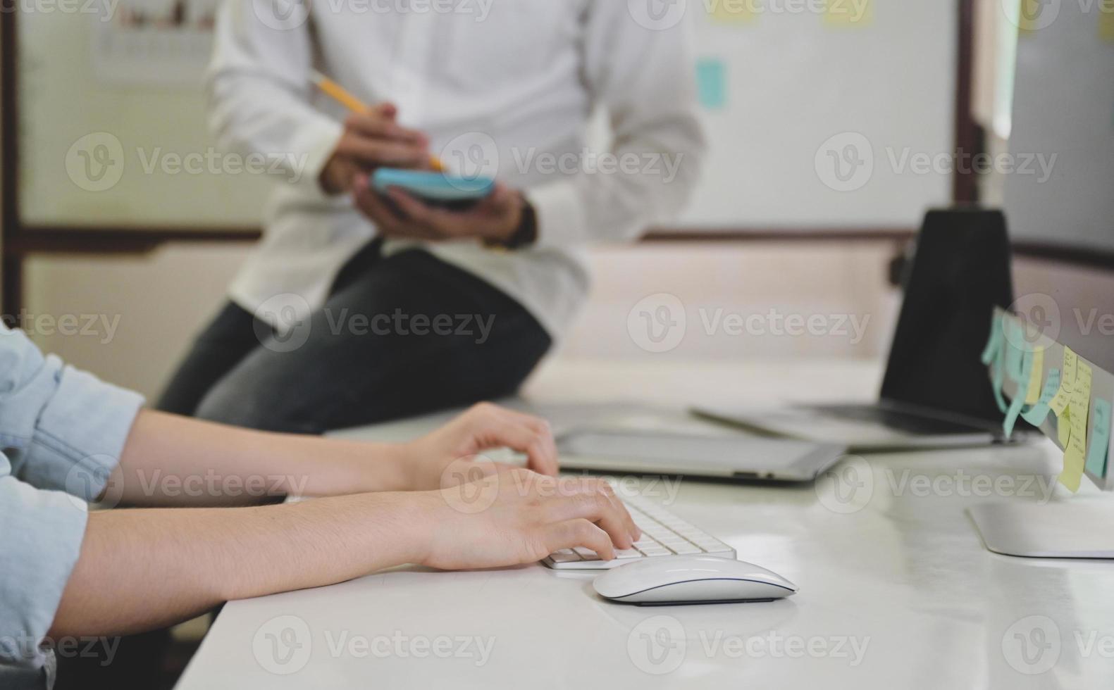 mani che lavorano sulla tastiera del computer e persone sedute sulla scrivania. foto