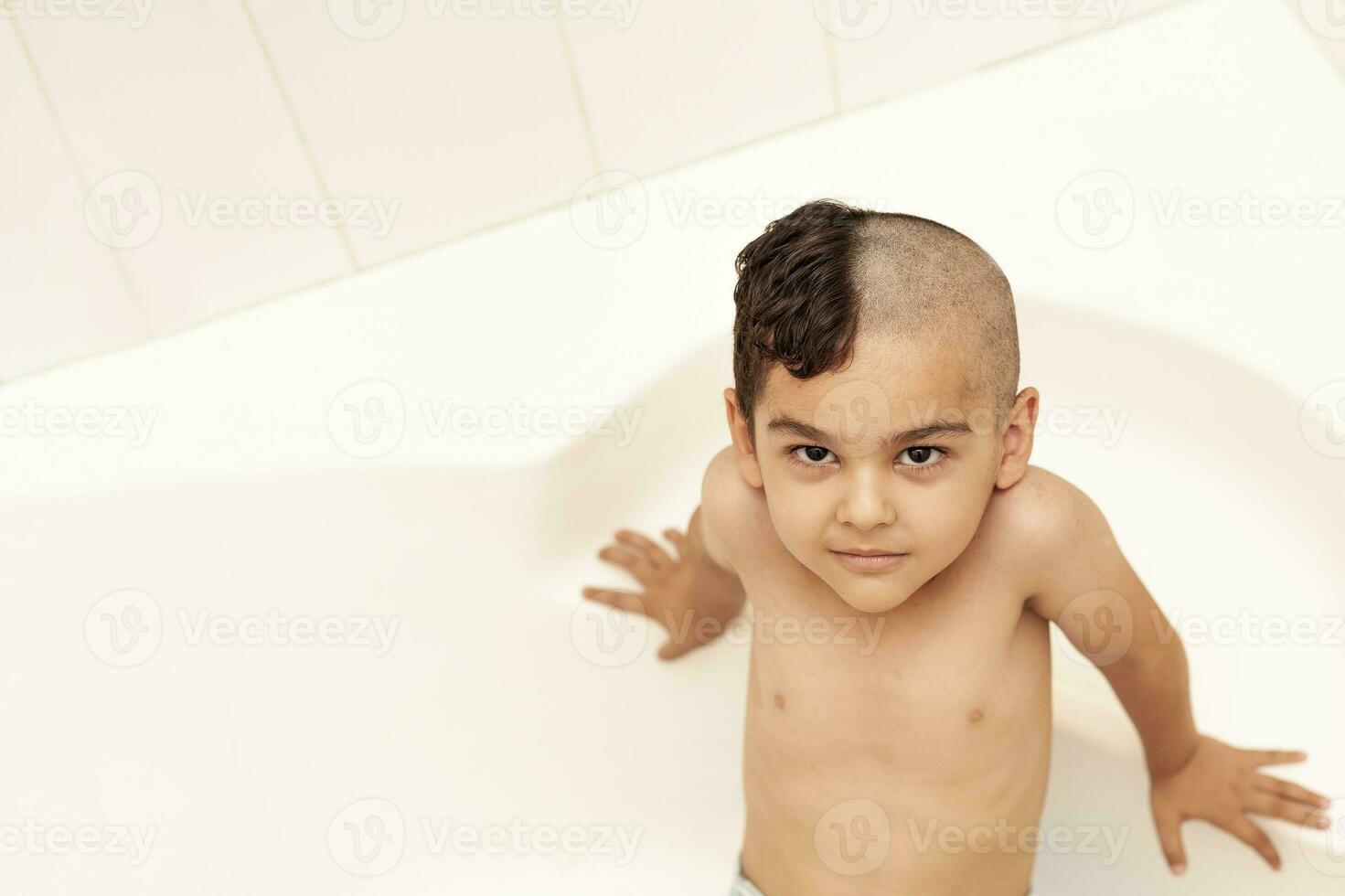 sei anni ragazzo a taglio di capelli a casa. padre tagliare metà di il figli maschi capelli via a il bagno foto