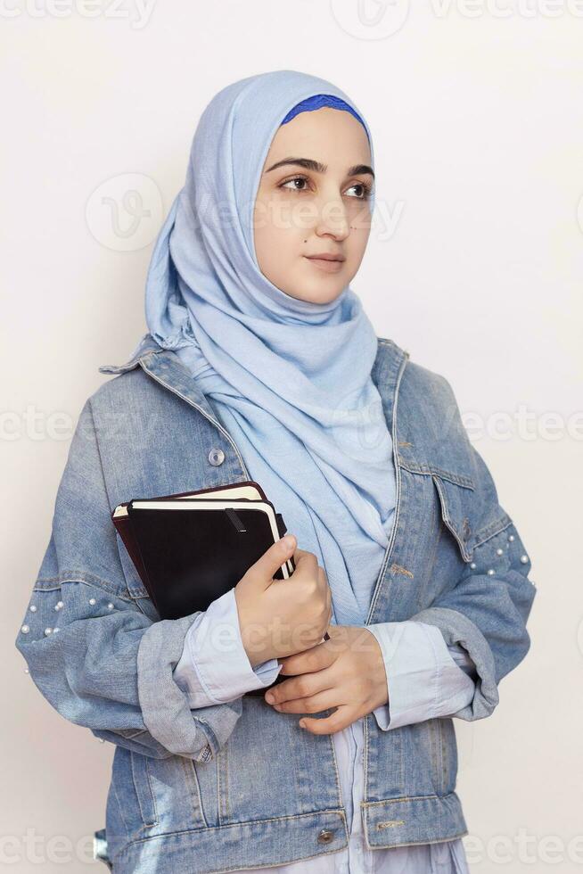 ritratto di carino musulmano donna d'affari. attraente musulmano alunno Tenere taccuini. bello musulmano ragazza nel hijab e denim giacca. moderno, culturale, religioso e attività commerciale concetto foto