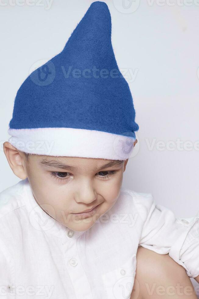 un' poco ragazzo fabbricazione un' divertente infastidito viso. infastidito Natale ragazzo nel Santa cappello. un' veramente grave e bello ragazzo foto