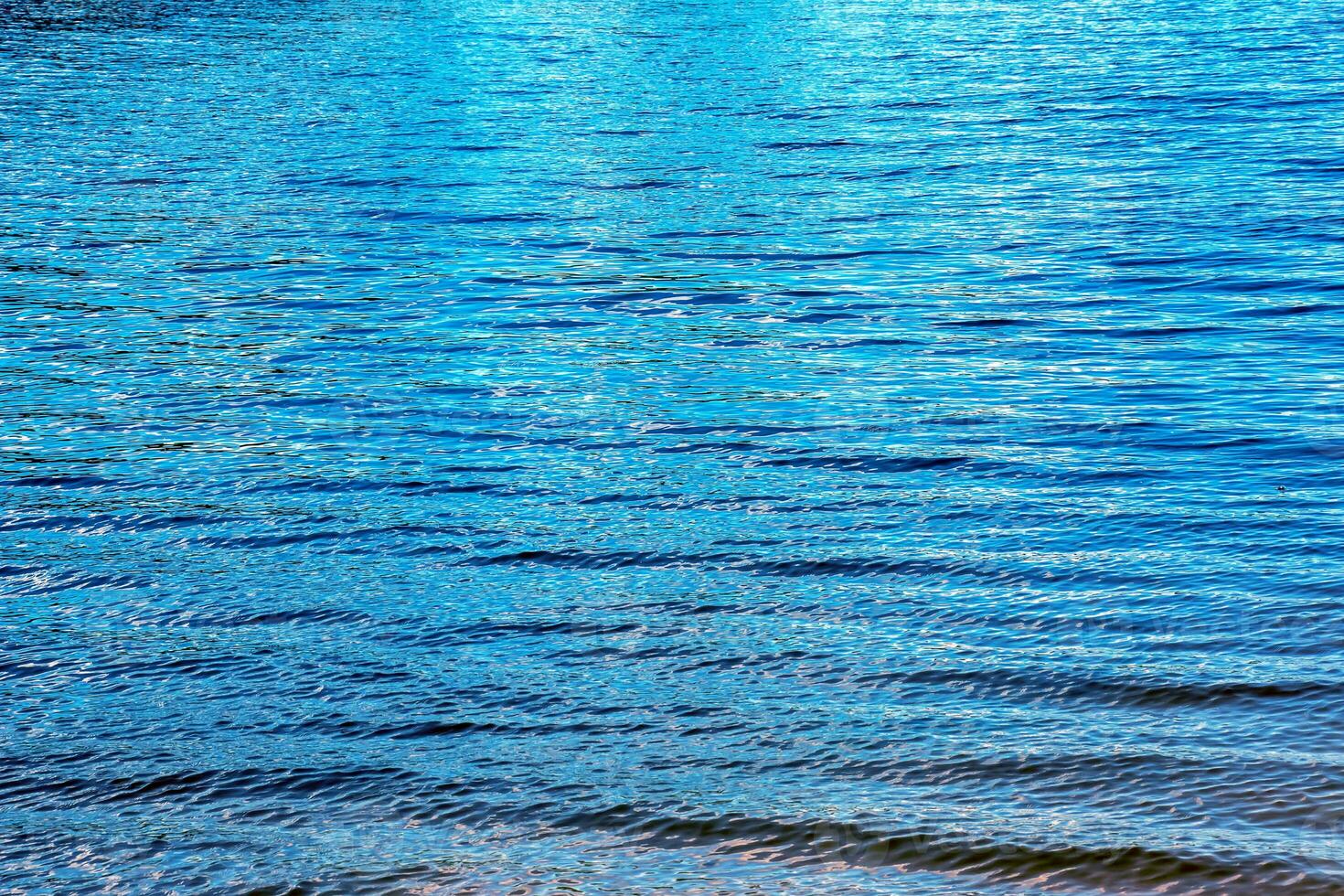 acqua ondulazione struttura sfondo. ondulato acqua superficie durante tramonto, d'oro leggero riflettendo nel il acqua. foto