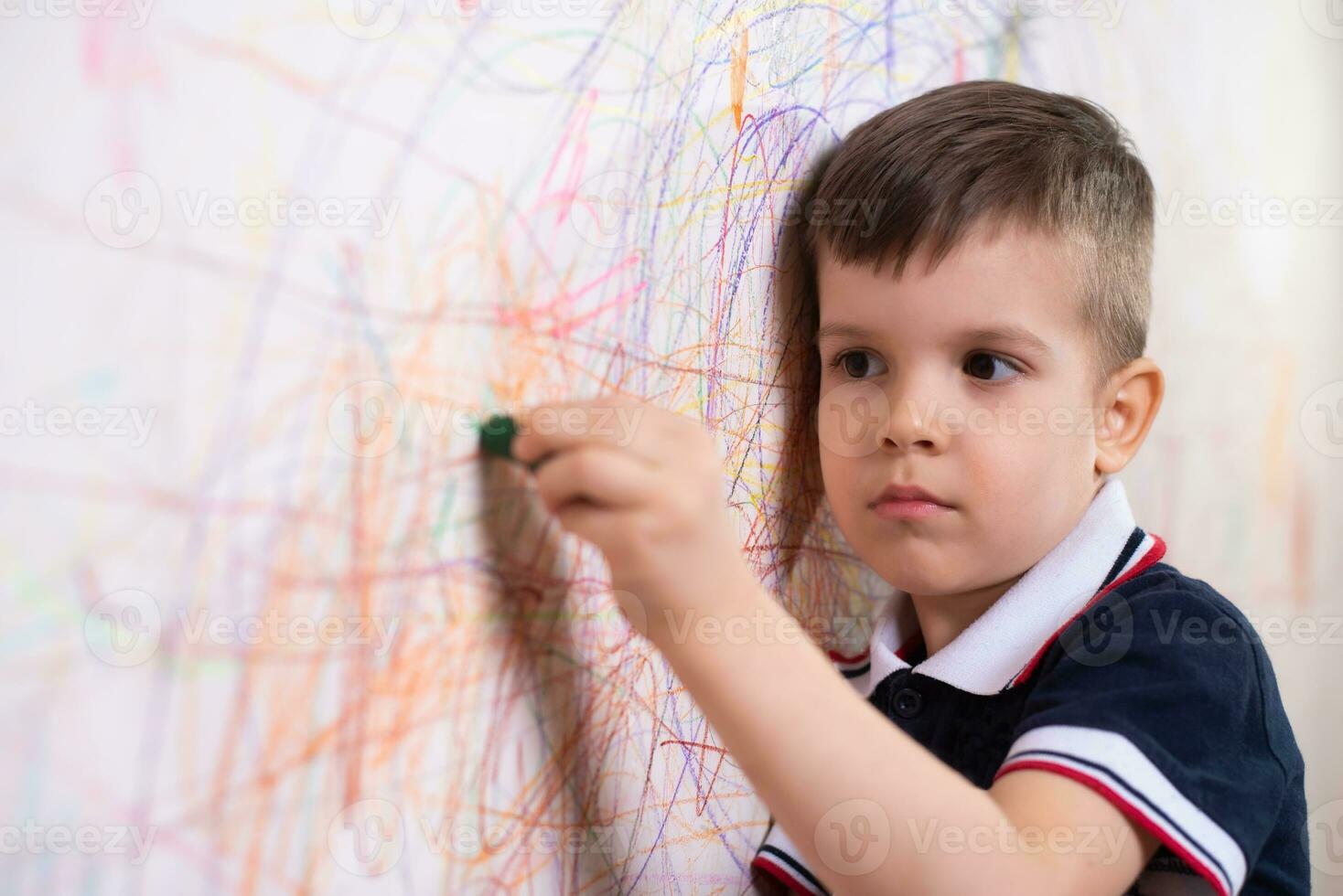 il bambino disegna su il parete con un' pastello. il ragazzo è impegnato nel creatività a casa foto