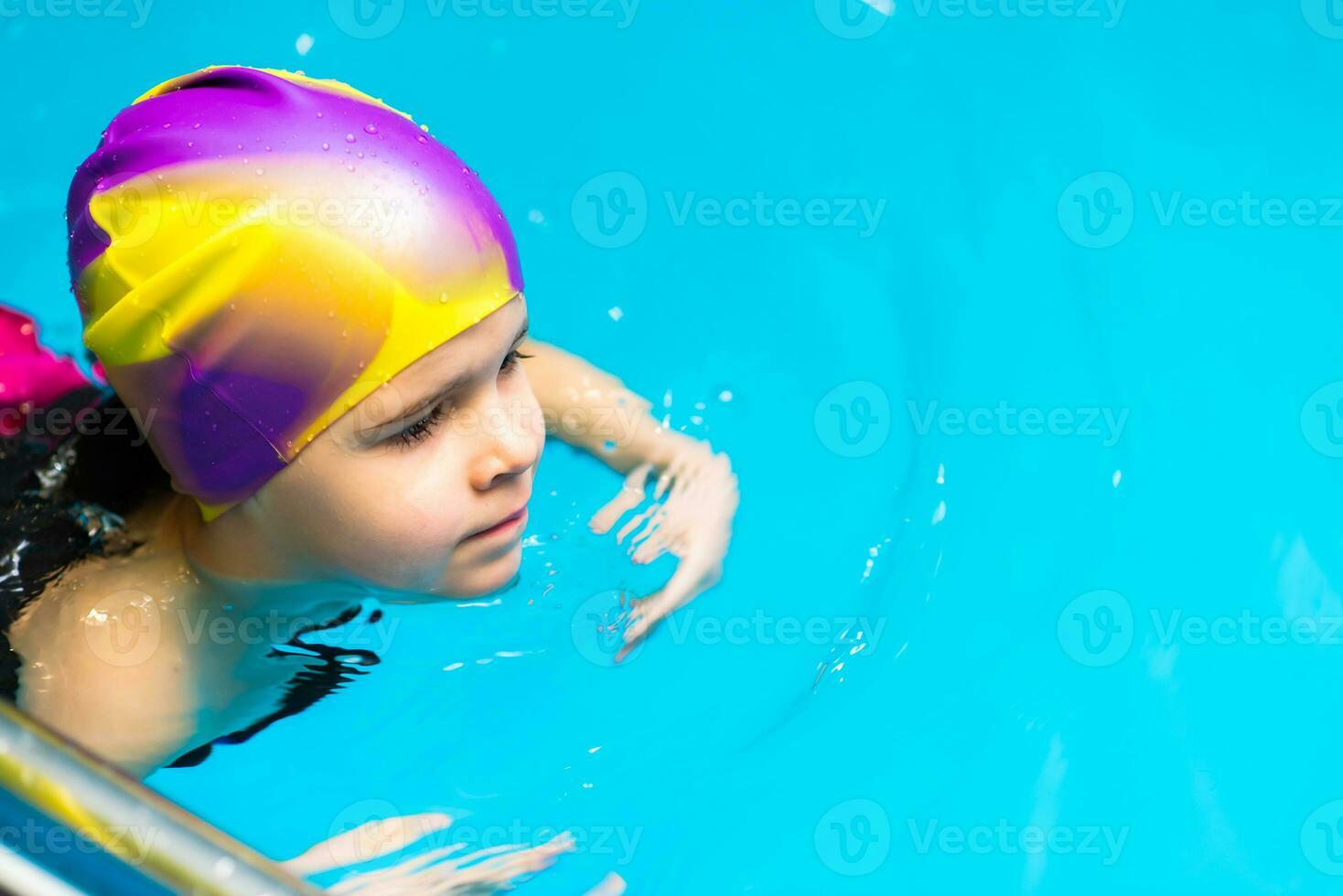 un' piccolo bambino con un' vita giacca su il suo il petto è apprendimento per nuotare nel un interno piscina. foto