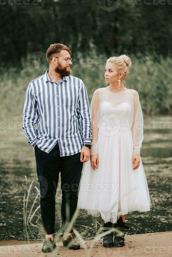 bellissimo appena sposato In piedi su il sfondo di il lago e posa. foto