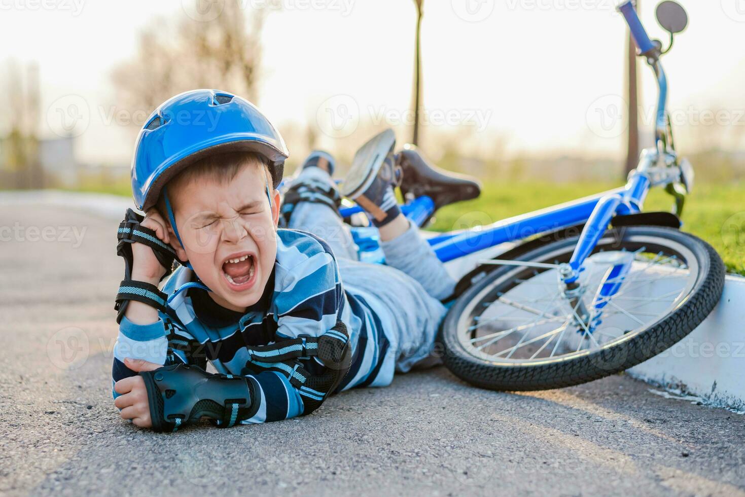 un' piccolo bambino abbattere a partire dal un' bicicletta su il strada, pianto e urlando nel dolore. foto