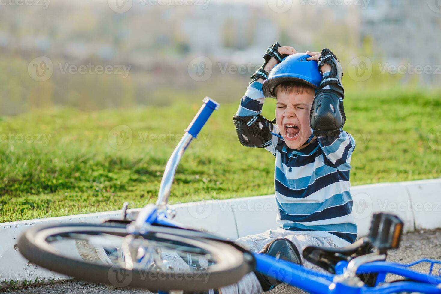 un' piccolo bambino abbattere a partire dal un' bicicletta su il strada, pianto e urlando nel dolore. foto