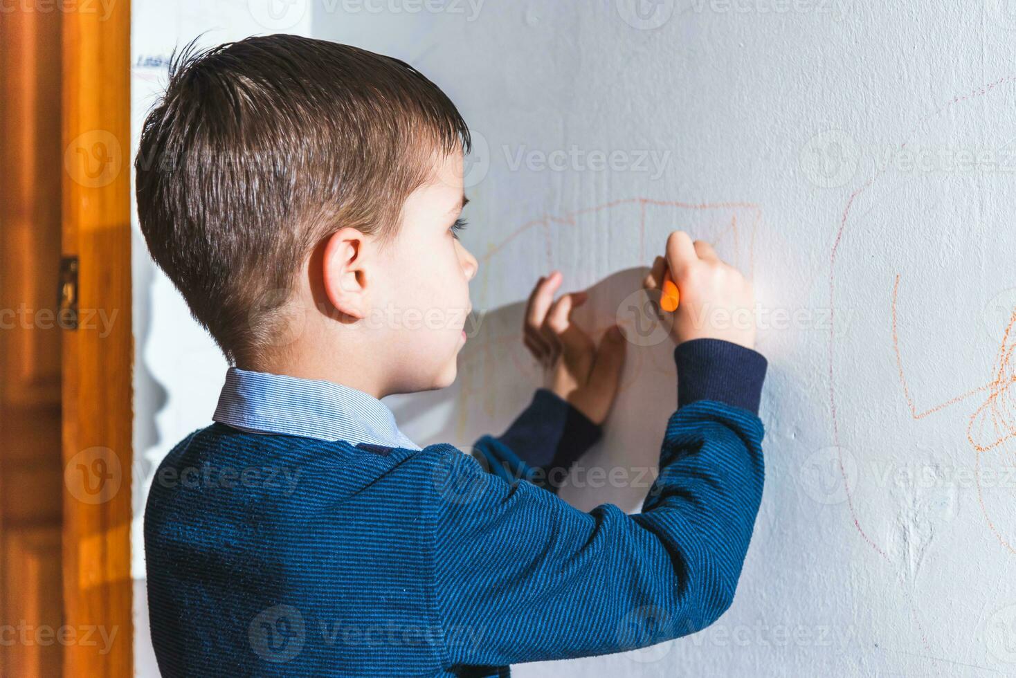 il bambino disegna su il parete con un' pastello. il ragazzo è impegnato nel creatività a casa foto