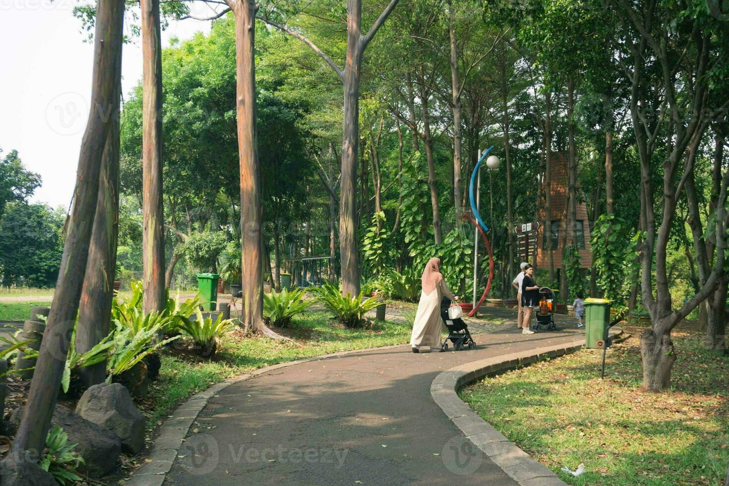 giovane hijab madre con poco figlia con passeggino a piedi insieme. mamma passeggiate nel il parco con sua figlia e detiene sua nel sua braccia. Visualizza a partire dal il indietro foto