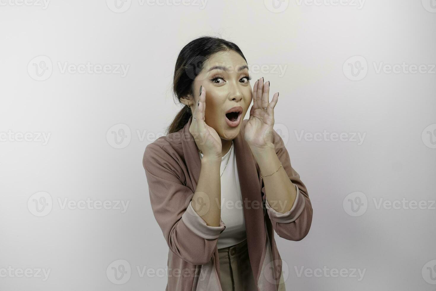 un' giovane bellissimo asiatico donna dipendente indossare cardigan è urlando e urlando forte con un' mano su sua bocca, isolato di bianca sfondo. foto