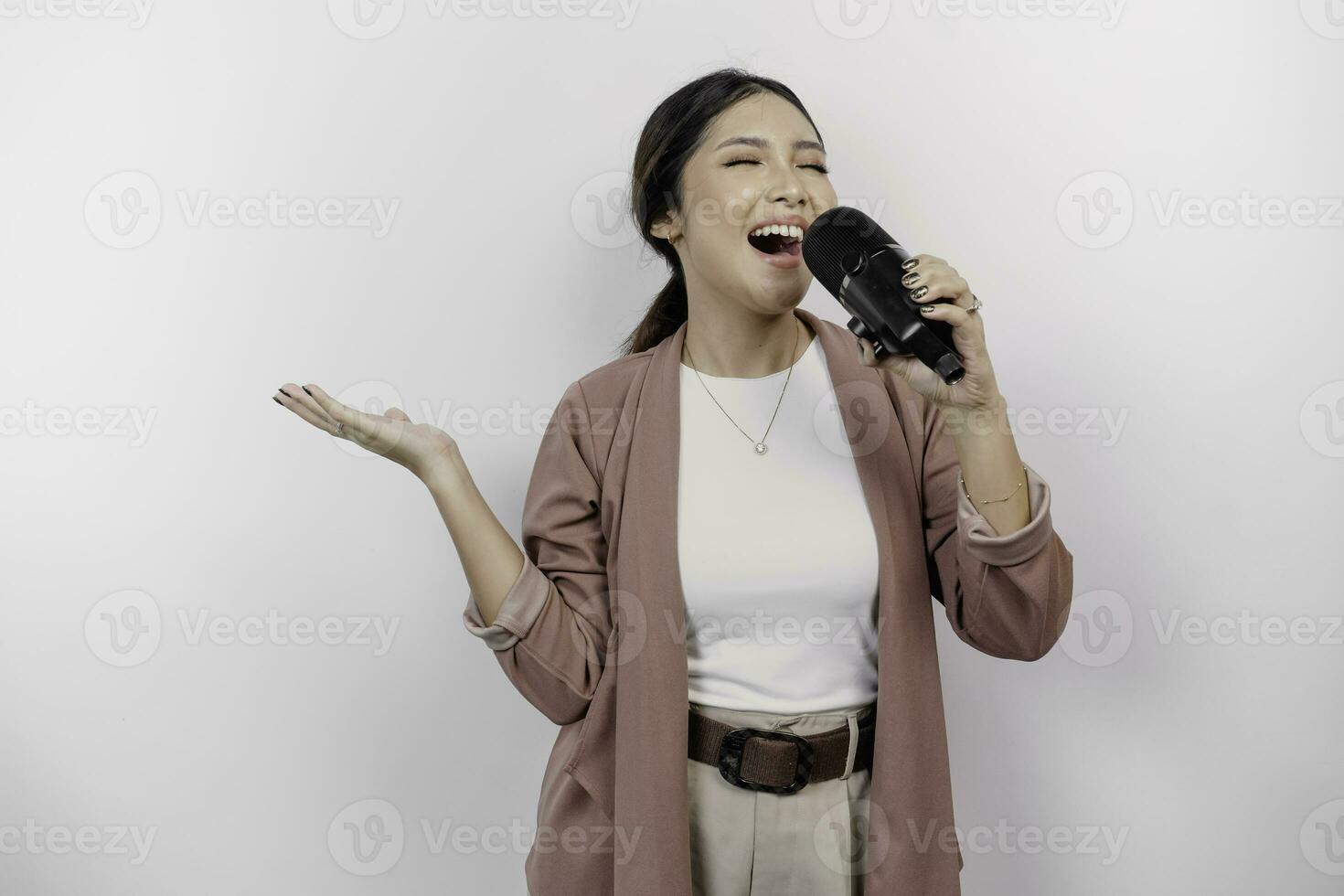 spensierato asiatico donna è avendo divertimento karaoke, cantando nel microfono mentre in piedi al di sopra di bianca sfondo foto