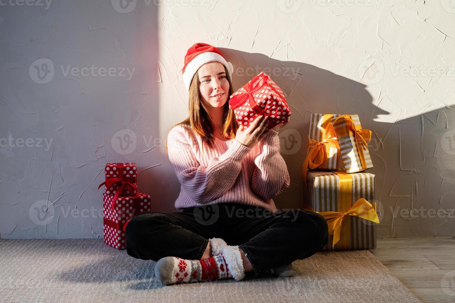 giovane donna con cappello da Babbo Natale circondata da regali foto