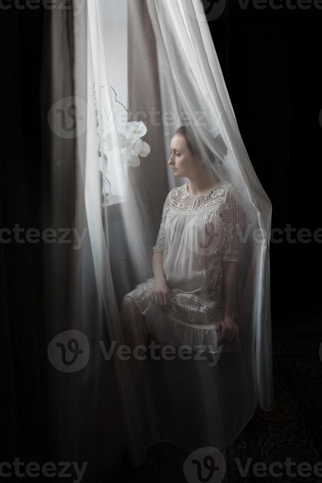 donna incinta dietro una tenda bianca foto
